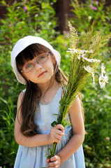 Wall Mural - Cute girl in glasses with bouquet of grass and daisies