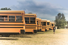 Back Of Many Yellow Schools Bus With A Cloudy Sky.
