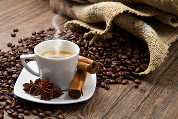 Coffee cup with burlap sack of roasted beans on rustic table