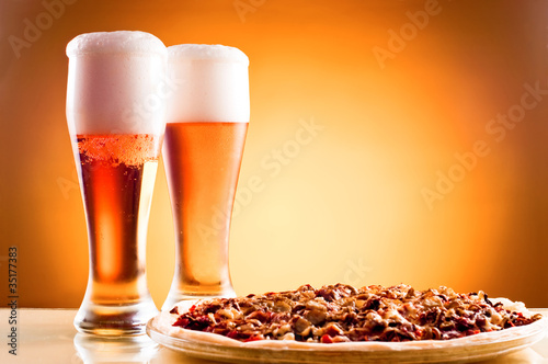 Board z aluminiowym obramowaniem Dwie szklanki piwa i pizza na żółtym tle