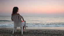 Woman Sits On Chair Alone On Beach And Looks In Distance Pensive