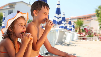 Wall Mural - Boy and girl eat ice cream on beach, then he licks his hand