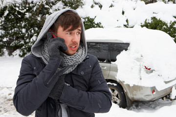 Young man in snow with broken down car