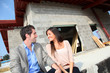 © goodluz - Happy couple sitting in front of house under construction