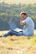 © Evgeniya Uvarova - young man using laptop sitting on the grass on the hillside