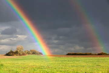 natural two rainbow over green field and dark sky