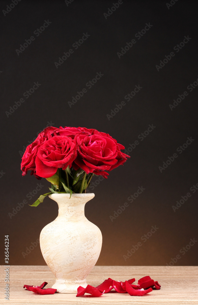 Beautiful red roses in vase on wooden table on brown background
