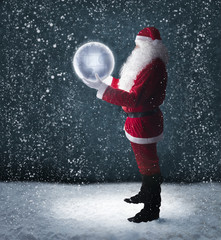 Santa Claus holding glowing planet earth under falling snow