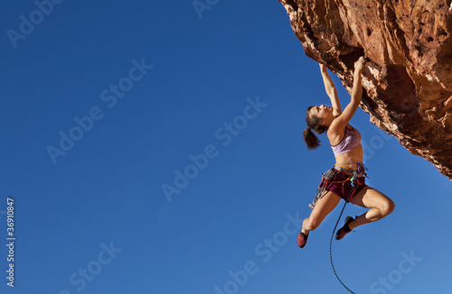 Fotografia, Obraz  Female climber clinging to a cliff.