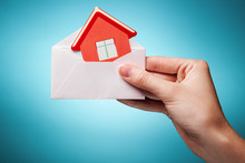 Woman's Hand Holding An Envelope With A Sign Of The House Agains