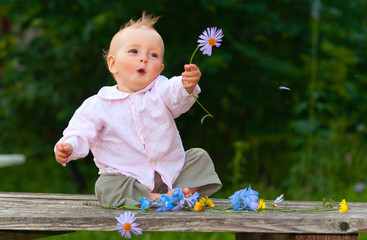 Adorable one-year baby sitting on the table with flowers and smi