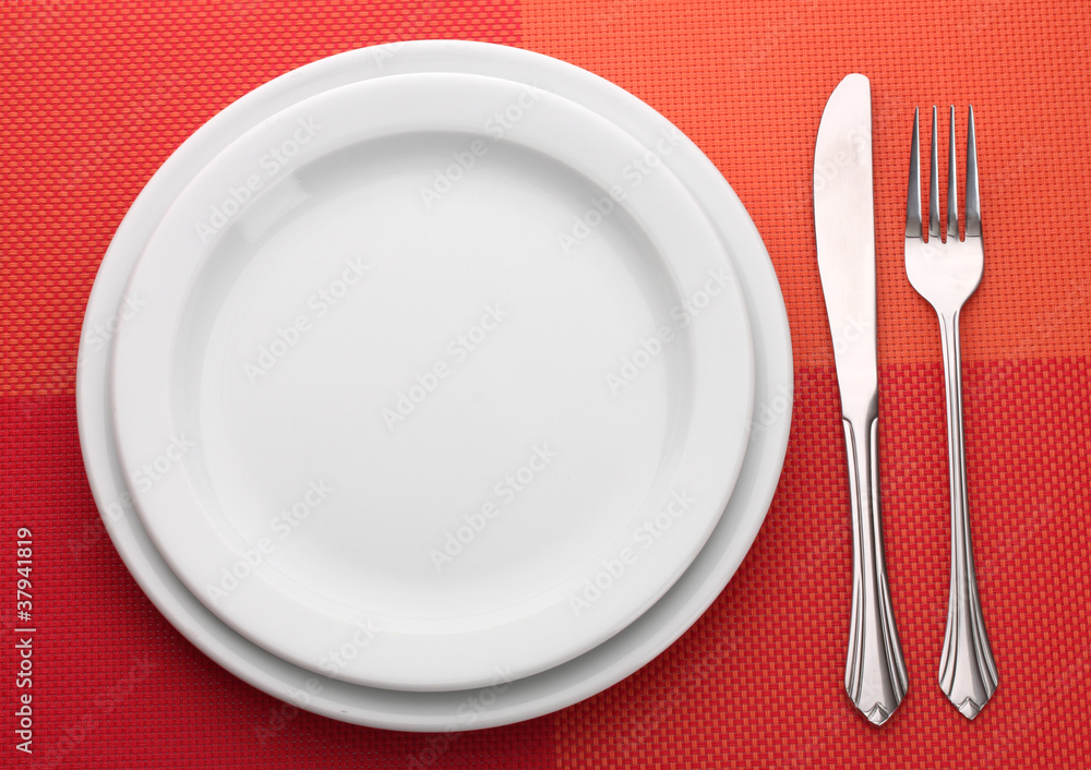 White empty plate with fork and knife on a red tablecloth