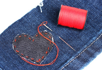 heart-shaped patch on jeans wiht needle and thread closeup