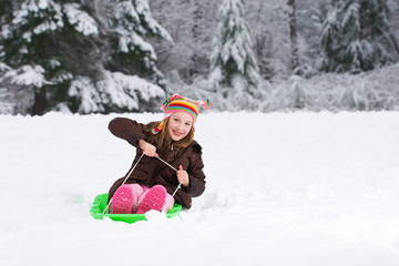 Wall Mural - Young girl playing on a snow sled