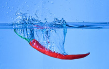 Red Pepper Dropped Into Water With Splash On Blue