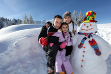 Couple Posing With Child Beside Snowman At Mountain Resort