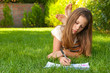 © Solid photos - Cute teenage girl lies on the grass and draws in her notebook