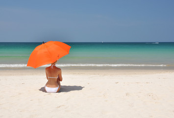 Wall Mural - Girl with an orange umbrella on the sandy beach