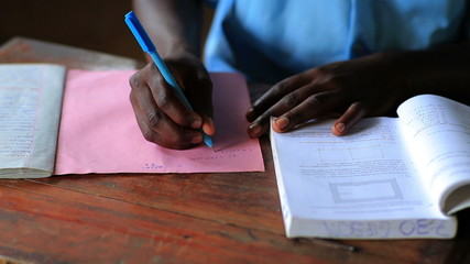 Wall Mural - Close up of hands of a school boy doing education homework in Kenya, Africa.