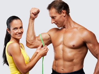 Woman measuring athletic's man biceps.