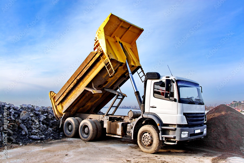 Dump truck is dumping gravel on an excavation site - obrazy, fototapety, plakaty 
