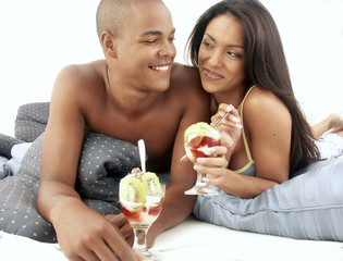 Pareja latina compartiendo y comiendo ensalada de frutas.