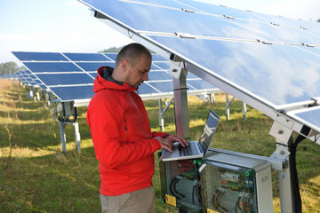 engineer using laptop at solar panels plant field