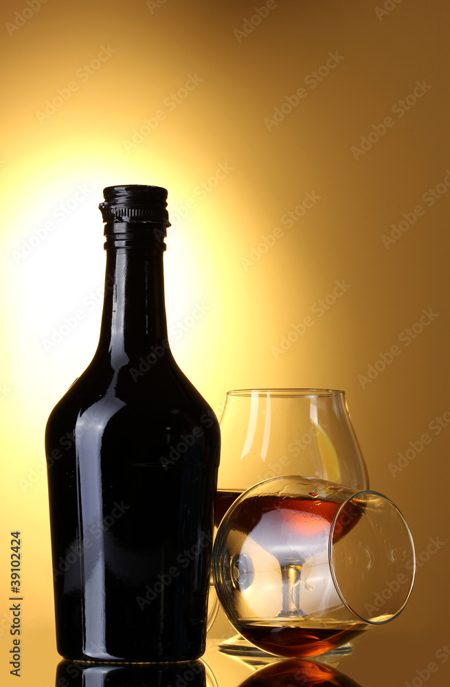 Glasses of brandy and bottle on yellow background