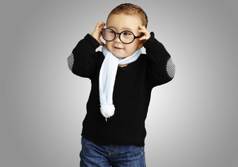 portrait of funny kid holding his glasses  against a grey backgr