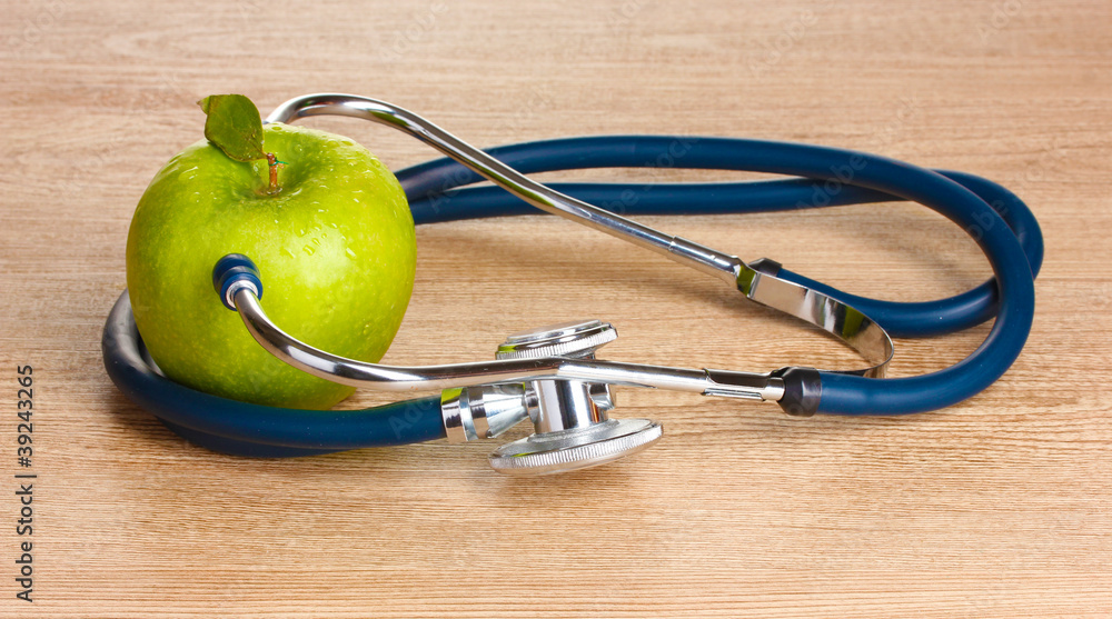 Medical stethoscope and green apple on wooden background