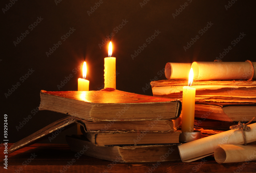 Pile of old books with candle and scroll in dark