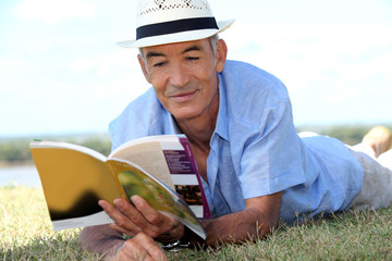 elderly gentleman lying on grass reading tourist guide