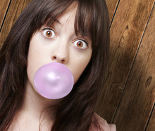 Young Girl With A Pink Bubble Of Chewing Gum Against A Wooden Ba