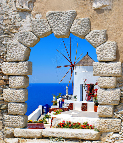 Fototapeta na wymiar Windmill through an old window in Santorini island, Greece