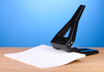 black office hole punch with paper on blue background