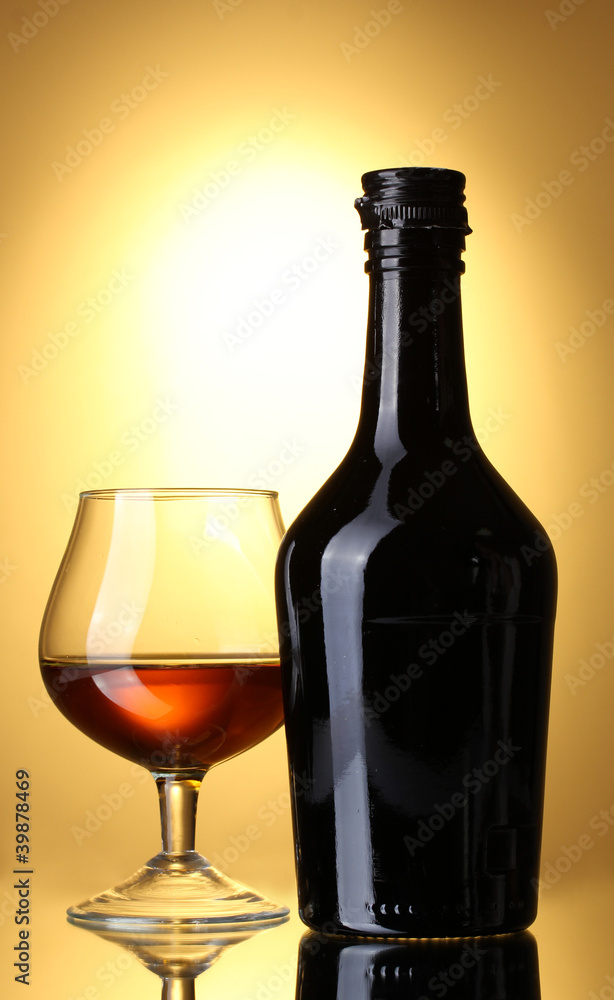 Glass of brandy and bottle on yellow background