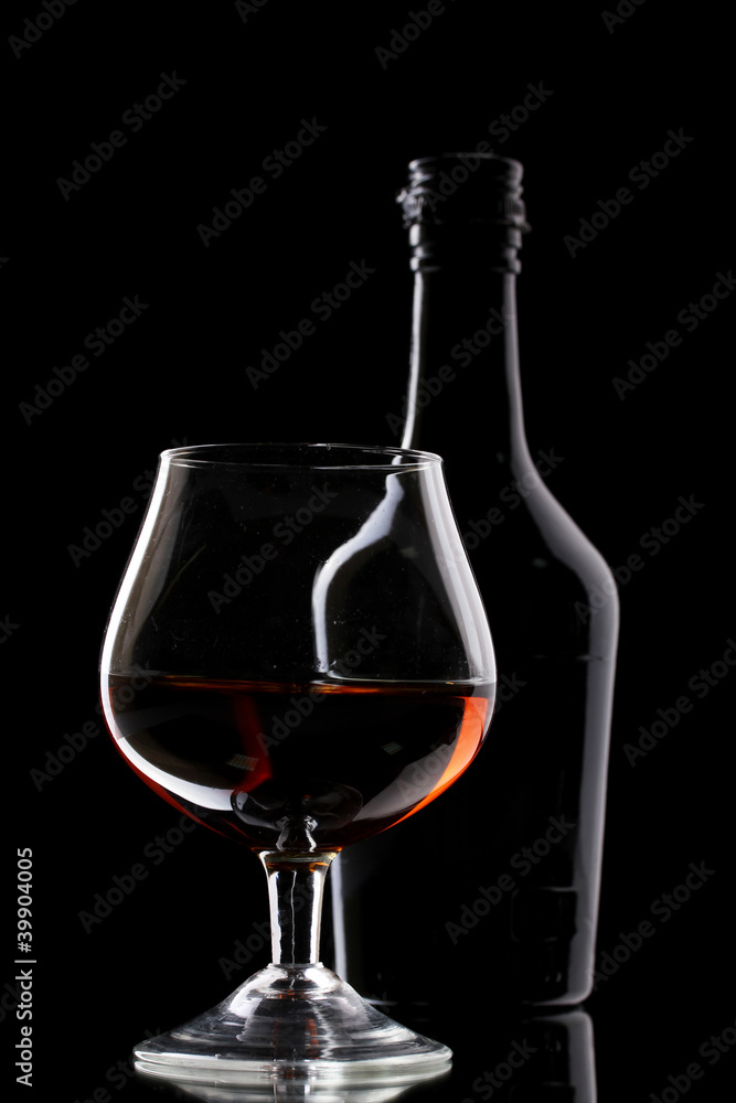 Glass of brandy and bottle on black background