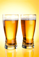 Two glasses of beer close-up with froth over yellow background