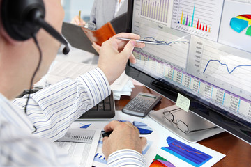 Fototapete - Man on a phone analyzing financial data on computer