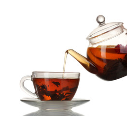 Glass teapot pouring black tea into cup isolated on white