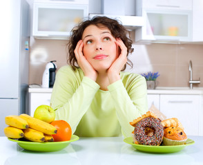 Wall Mural - Beautiful Young Woman choosing between Fruits and Sweets