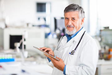 Senior doctor using his tablet computer at work (color toned ima