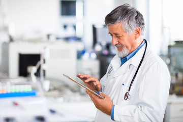 Senior doctor using his tablet computer at work (color toned ima