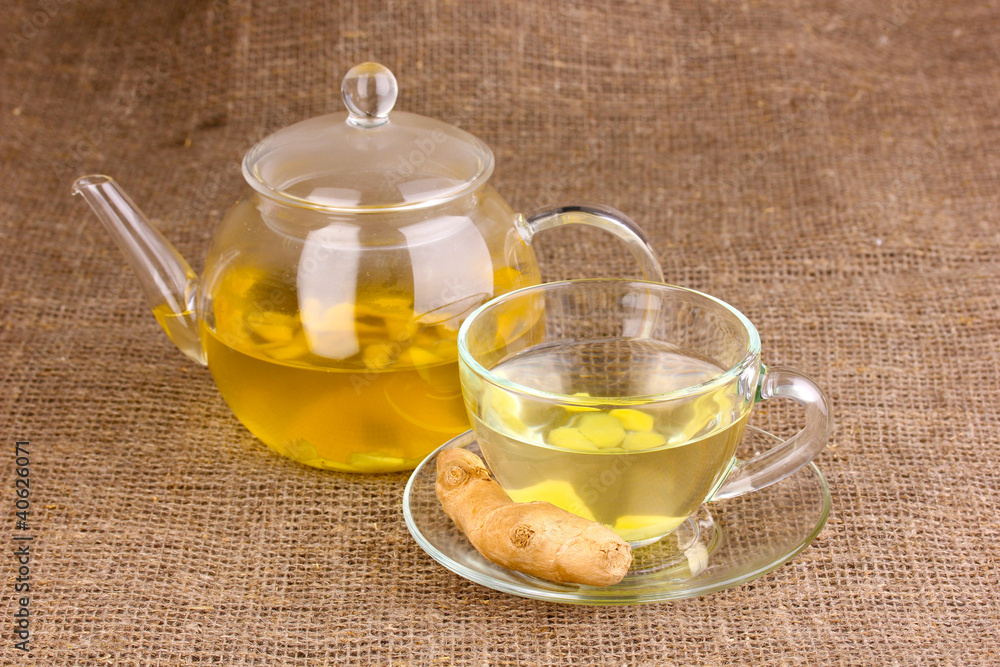 Healthy ginger tea in kettle and cup on sackcloth