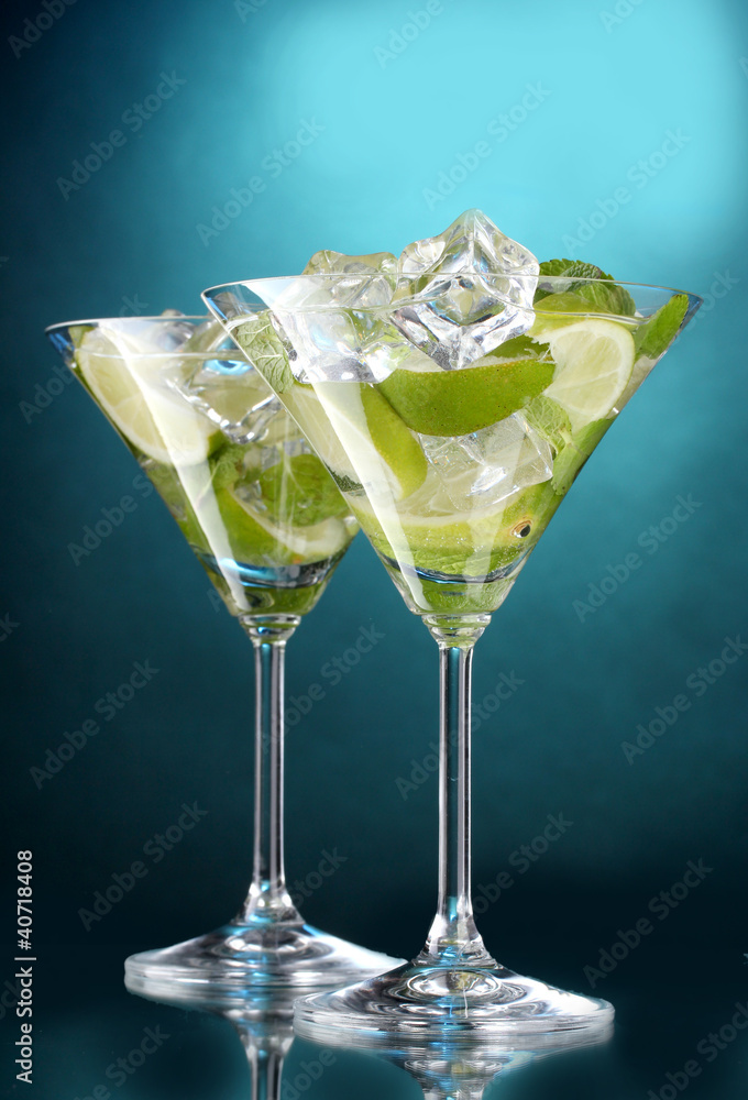 glasses of cocktails with lime and mint on blue background