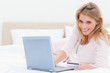© WavebreakmediaMicro - Woman lying on the bed, with a laptop in hand and looking forwar