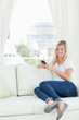 © WavebreakmediaMicro - A woman sitting sideways on the couch as she uses her phone