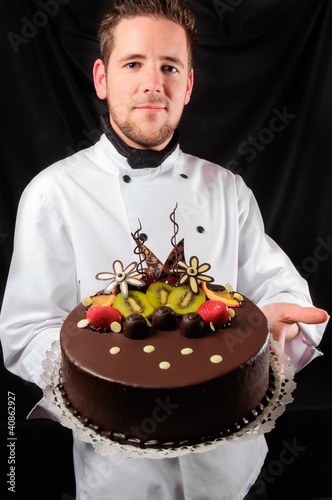 Fotoboard na płycie Przystojny szef kuchni z ciastem na ciemnym tle