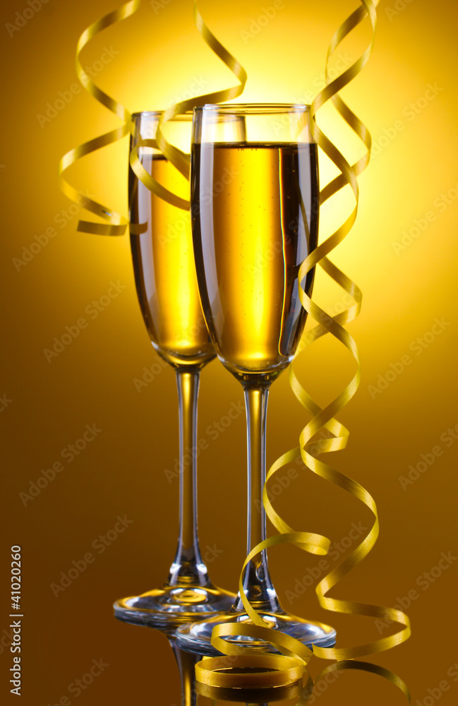 glasses of champagne and streamer on yellow background