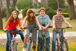 © Solid photos - Four happy teenage friends riding bicycles in the park